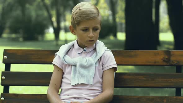 Unhappy Little Boy Sitting Alone on Bench in Park, School Bullying and Cruelty alt