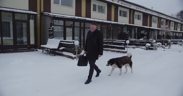 A Man With A Briefcase Rides Down A Snowy Street, Followed By A Large Dog
