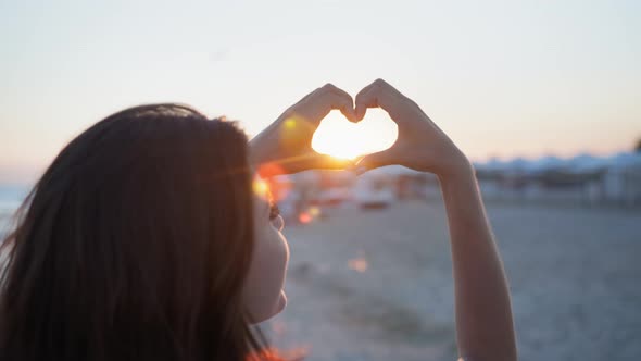 Rest By Sea, Young Happy Girl Shows Love Heart with Hands on Background of Sun on Beach During