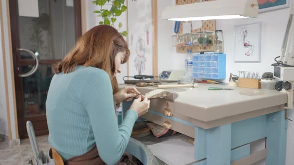 Back View Of A Female Jewelry Maker Filing A Piece Of Jewellery In A Workshop alt