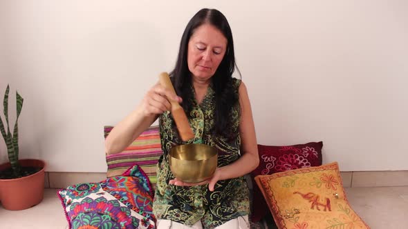 Middle age woman using bronze Tibetan singing bowl. Concept of relax and zen aura. alt