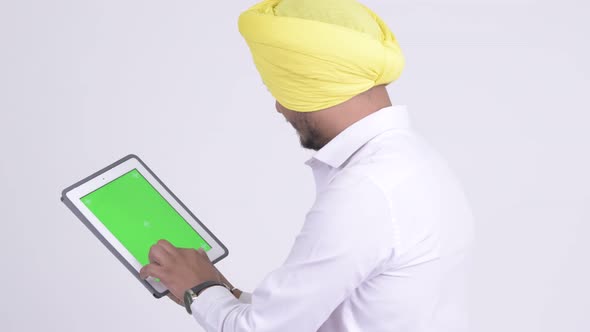 Rear View of Bearded Indian Sikh Businessman Using Digital Tablet alt