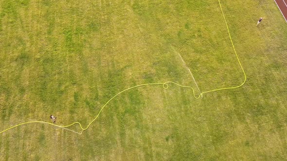 Top down aerial view of football field surface covered with green grass and sprinklers spraying alt