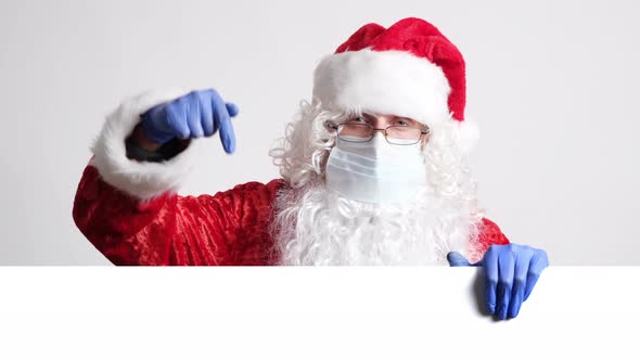 Santa Claus in Surgical Mask and Gloves Pointing Down on a Place Where You Can Add Your Message