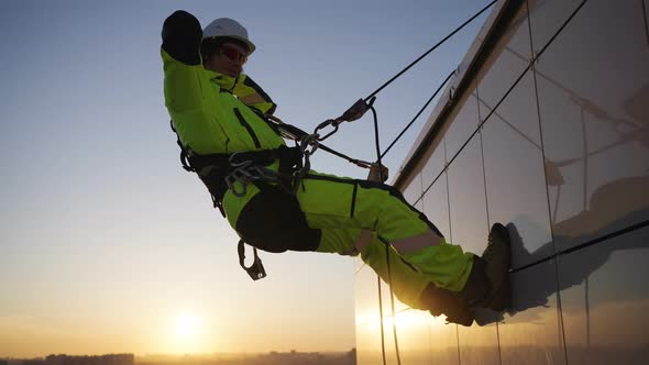 Funny Industrial Climber Cute Dancing Hanging on the Ropes at a Height Against the Background of the alt