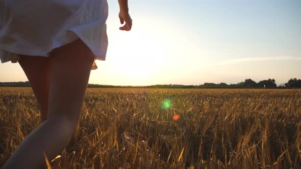 Unrecognizable Joyful Woman in White Dress Running Through Field of Wheat at Sunset alt