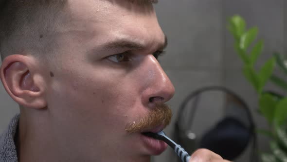 Young caucasian man is brushing teeth with toothbrush in modern bathroom in the morning.  alt