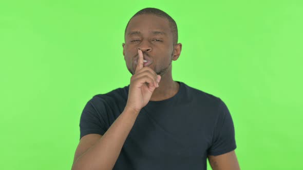 Silence Please Young African Man with Finger on Lips on Green Background alt