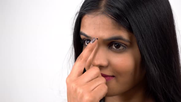 A beautiful and attractive Indian girl in an Indian ethnic outfit putting bindi on forehead alt