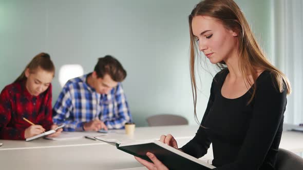 Portrait of a Young Female Student Reading a Book and Working on Her Homework While Her Friends are alt