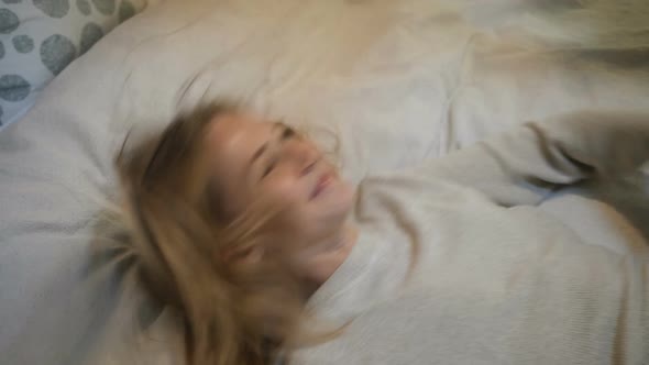 Woman in Sweater Falls Down Onto Large Bed in Light Room alt