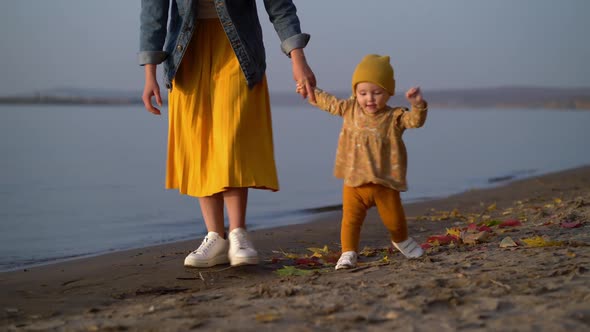 Mom Holds Her Daughter By the Hand and Teaches Her To Walk on Beach alt