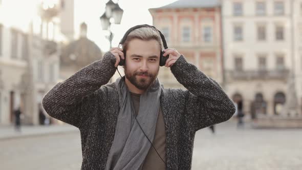 A Happy Bearded Man is Putting on Headphones and Looking at the Camera alt