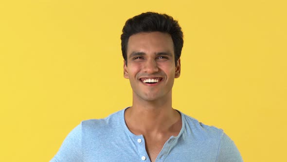 Young happy Indian man in plain gray t-shirt  laughing isolated on yellow background
