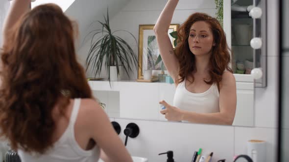 Caucasian woman applying spray antiperspirant in the bathroom. Shot with RED helium camera in 4K. alt