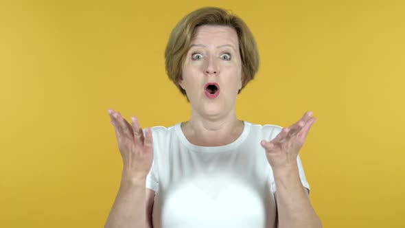 Happy Amazed Old Woman Surprised By Gift Isolated on Yellow Background alt