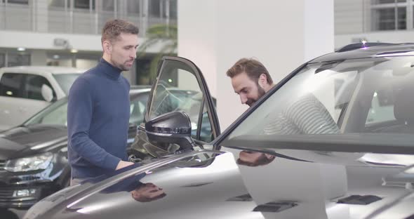 Male Caucasian Car Dealer Opening Car Door, Adult Man Sitting Into Salon alt