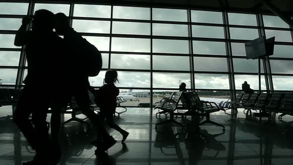 Travelers Walking Along Window in Airport Terminal, People Silhouettes Walking. alt