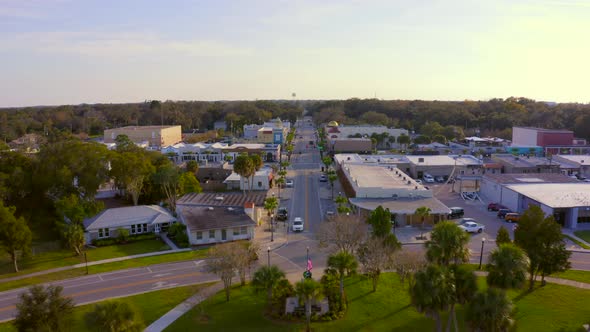Backwards Aerial Pan From Main Road of a Small Town to Trees Reflecting on Pond alt