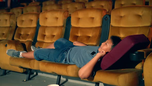 A Boy Laying Down on Armchair in Cinema alt