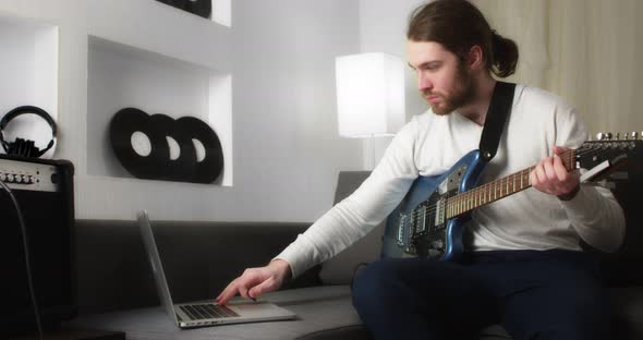 Young Man Watches an Instructional Video Guitar Lesson and Picks Up Notes