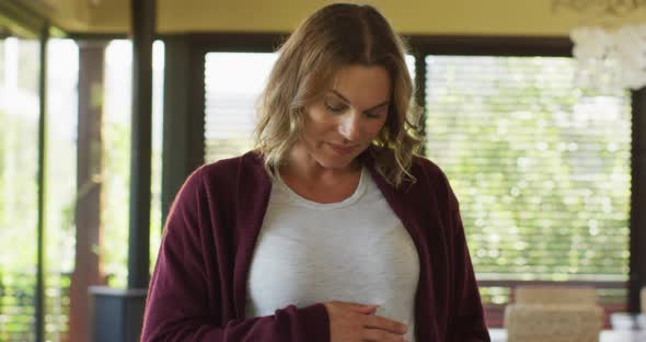 Portrait of happy caucasian pregnant woman touching belly and looking at camera alt
