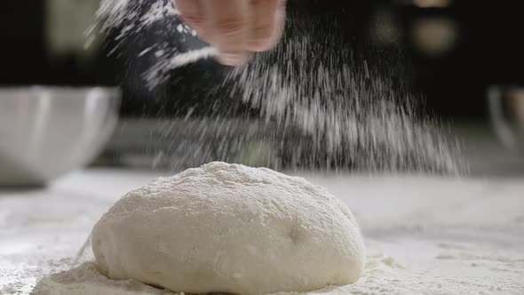 Baker in bakery makes morning dough for baking pizza sprinkles flour on dough