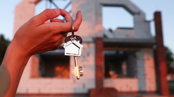 Hand with the key to the future house on the background of a construction site and walls alt
