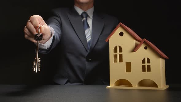 Businessman gives a keys near a house model on a table