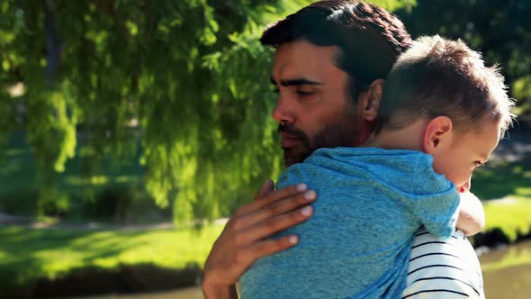 Father holding his sleeping son in park alt