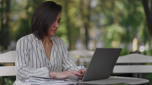 Business Woman Brunette Arabic Hispanic Ethnic Group is Typing on a Laptop While Sitting at a Table alt