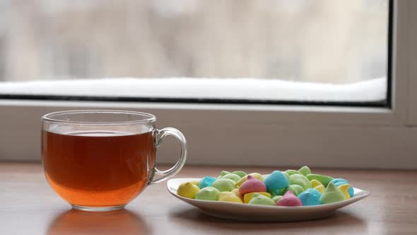 A Large Mug of Tea and Colorful Sweets in a Plate on the Windowsill By the Window in Winter