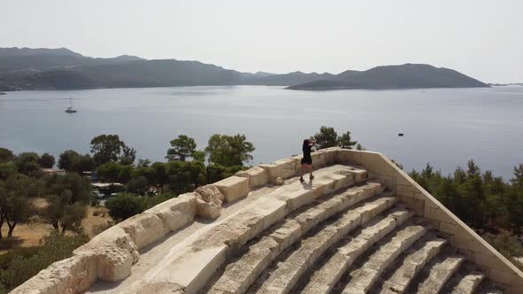 Beautiful girl walking in an antique Amphitheater with sea view in Kas, Turkey. Drone angle. alt