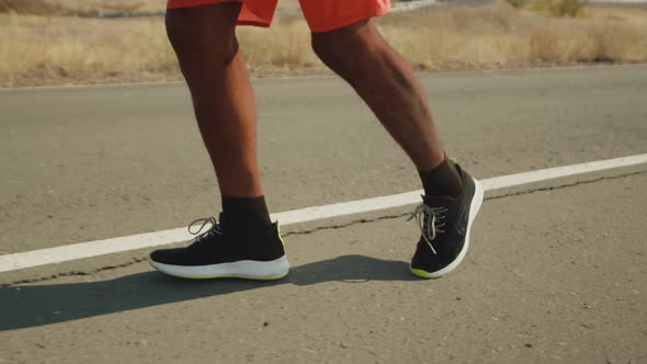 Black Legs of Athlete in Sneakers Confidently Run Along Road Closeup alt