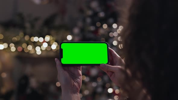 Close Up Woman Holding in Hands Cellphone Green Screen in Christmas Decoration