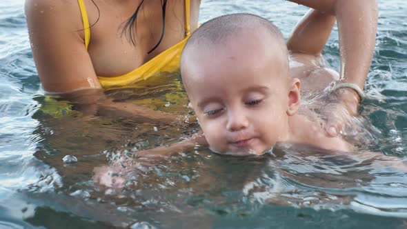 Handsome Cute Baby Boy Learning to Swim in the Sea His Mama is Holding Him alt