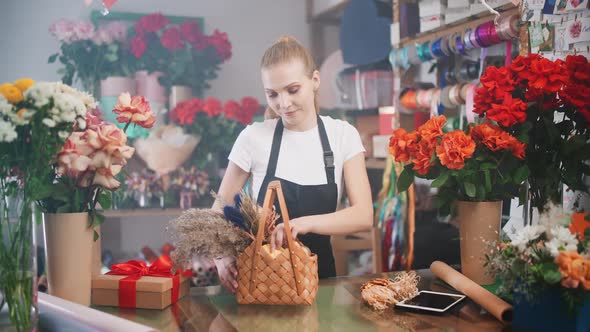 Young Florist Female Decorates a Bouquet of Dried Flowers in a Wicker Basket Cheerful Woman Working alt