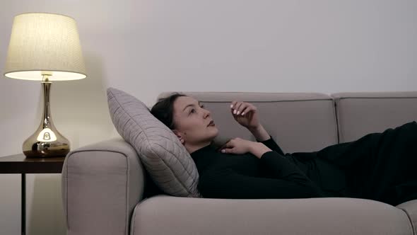 A Darkhaired Woman in a Dark Dress Lying Comfortably on a Sofa on a Pillow Enjoying a Rest in a alt