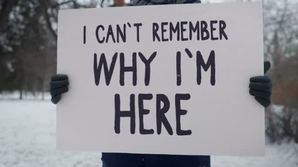 Person holds a white sign with I can't remember why i'm here statement. alt