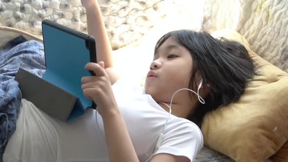 Asian Bored Boy Using Tablet While Lying On Bed alt