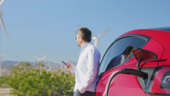 Caucasian Businessman Using Smartphone at Electric Vehicle Charging Station 6K alt