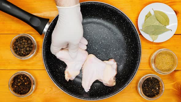 The cook puts the chicken wings in the pan. Chicken wings in a marble skillet, ready for marinating.