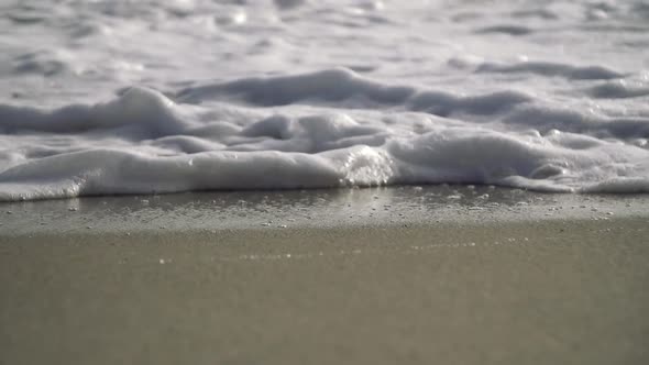Super slow motion close up of wave and bubbles crashing on the beach on a sunny day alt