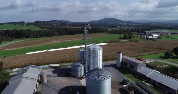 Aerial view pushing in towards American flag at top of grain silo with cornfields and mountains in t alt