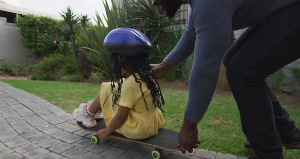 Happy african american father playing with daughter on skateboard in backyard alt