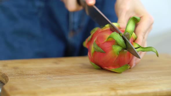 Female Hands is Cutting a Dragon Fruit or Pitaya with Pink Skin and White Pulp with Black Seeds on alt