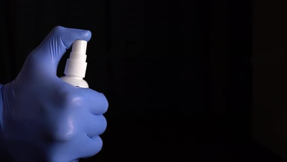 Medic In Blue Gloves Sprinkles With Antiseptic For Disinfection On Black Background