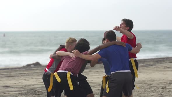 A group of guys playing flag football on the beach. alt