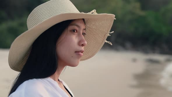 Attractive Asian girl wearing fedora hat standing on the beach looking at sea view beautiful sunset.