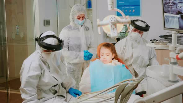 Little Patient in Ppe Suit Lying on Chair with Open Mouth During Dental Examination alt